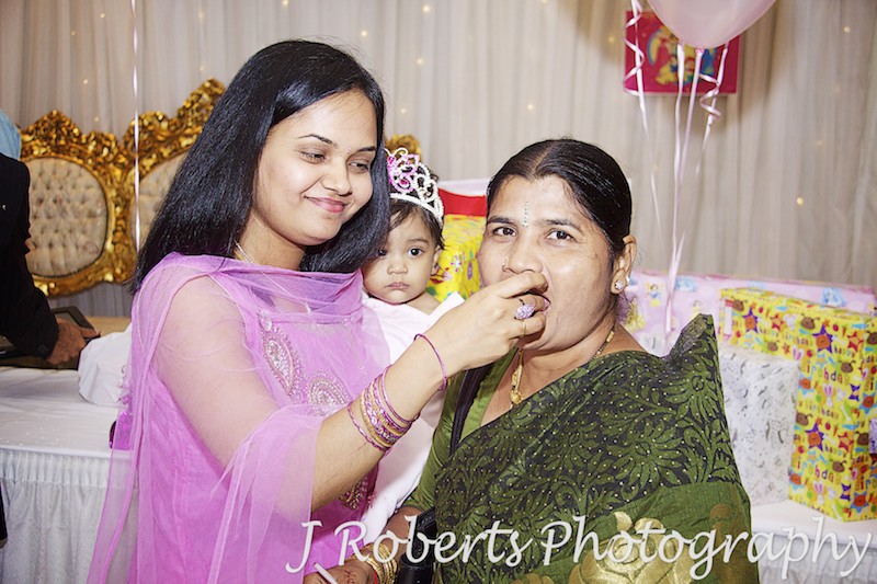Mother feeding grandmother cake at indian 1st birthday party - party photography sydney